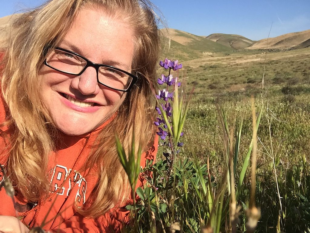 Julie JordanScott sits among lupine wildflowers. As the Creative Life Midwife, she also loves nature!