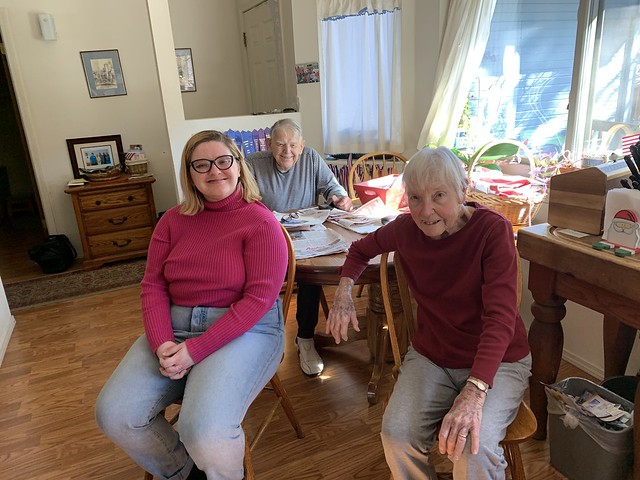 Two older people and their twenty-year-old granddaughter visit at the 
kitchen table, happy to see each other. 