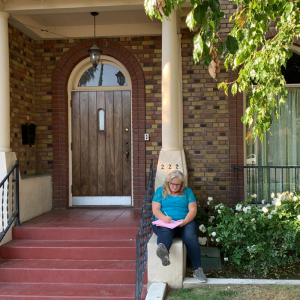Woman writing on the front porch of a brick home,