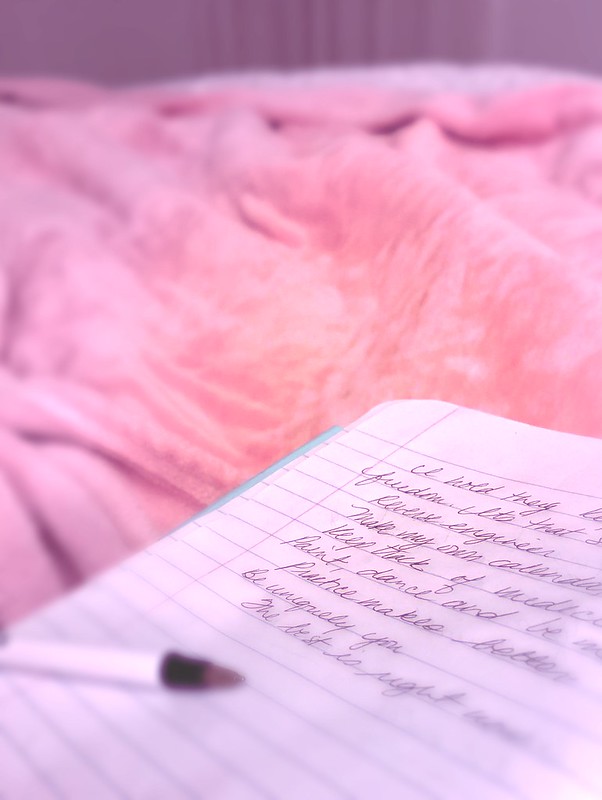 A writing notebook atop a pink bedspread to show the joy of writing in the early morning in bed. This is part of #rolloverandwrite