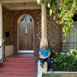 Woman writing on the front porch of a brick home, 