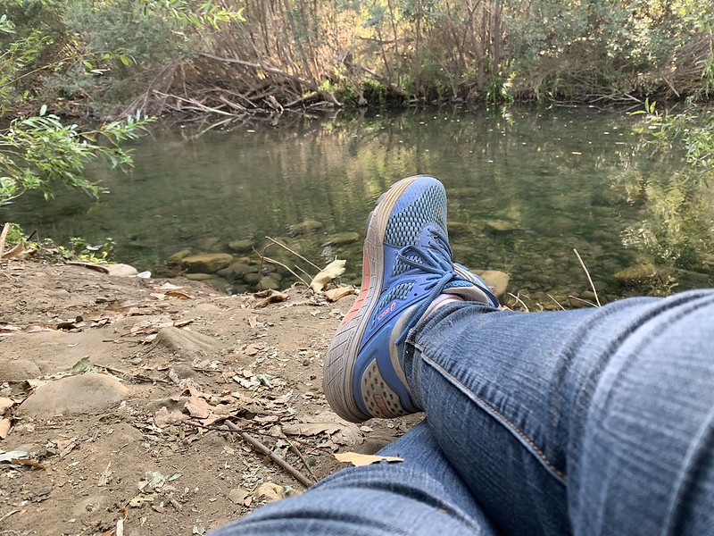 Woman's legs and shoes on the ground in front of a river. It is the writer of the blog, the Creative Life Midwife, practicing how to be a Warrior.