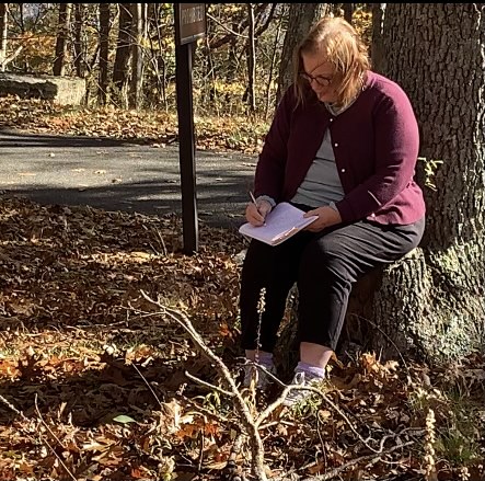 Woman sitting at the base of a tree, writing in her notebook. Julie Jordan Scott (Julie JordanScott) is the writer.